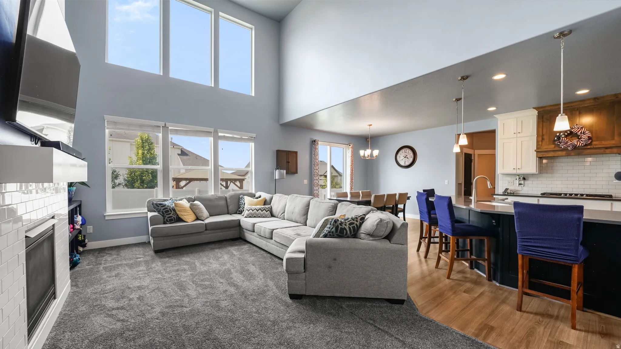 Vaulted ceilings with high windows, a fireplace with a subway tile surround, a kitchen island with pendant lighting, wood-finish flooring, and white kitchen cabinetry