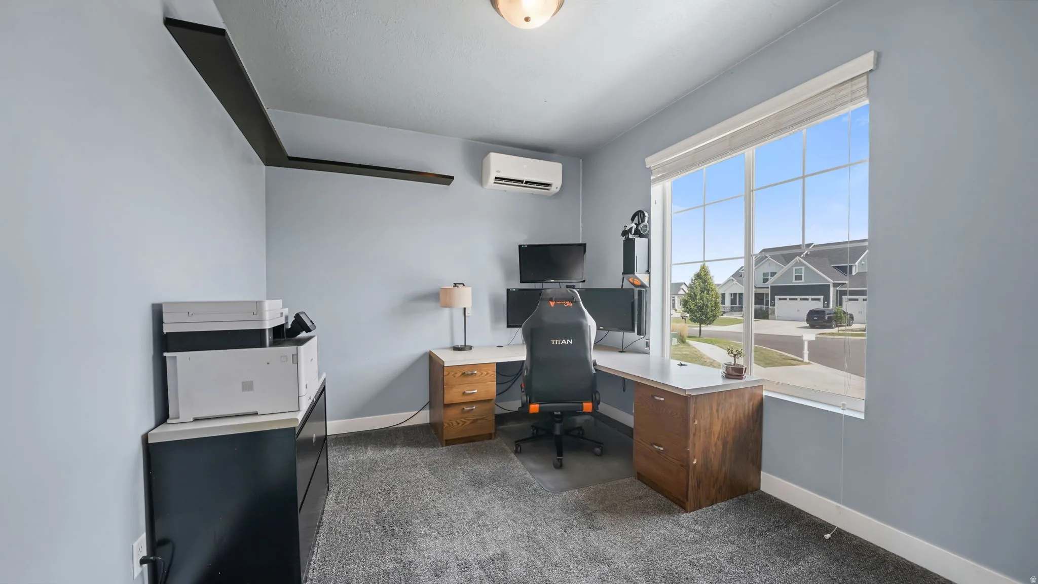 Wall-mounted AC unit, light gray wall paint, large window with grid pattern, white window blinds, and gray carpeting