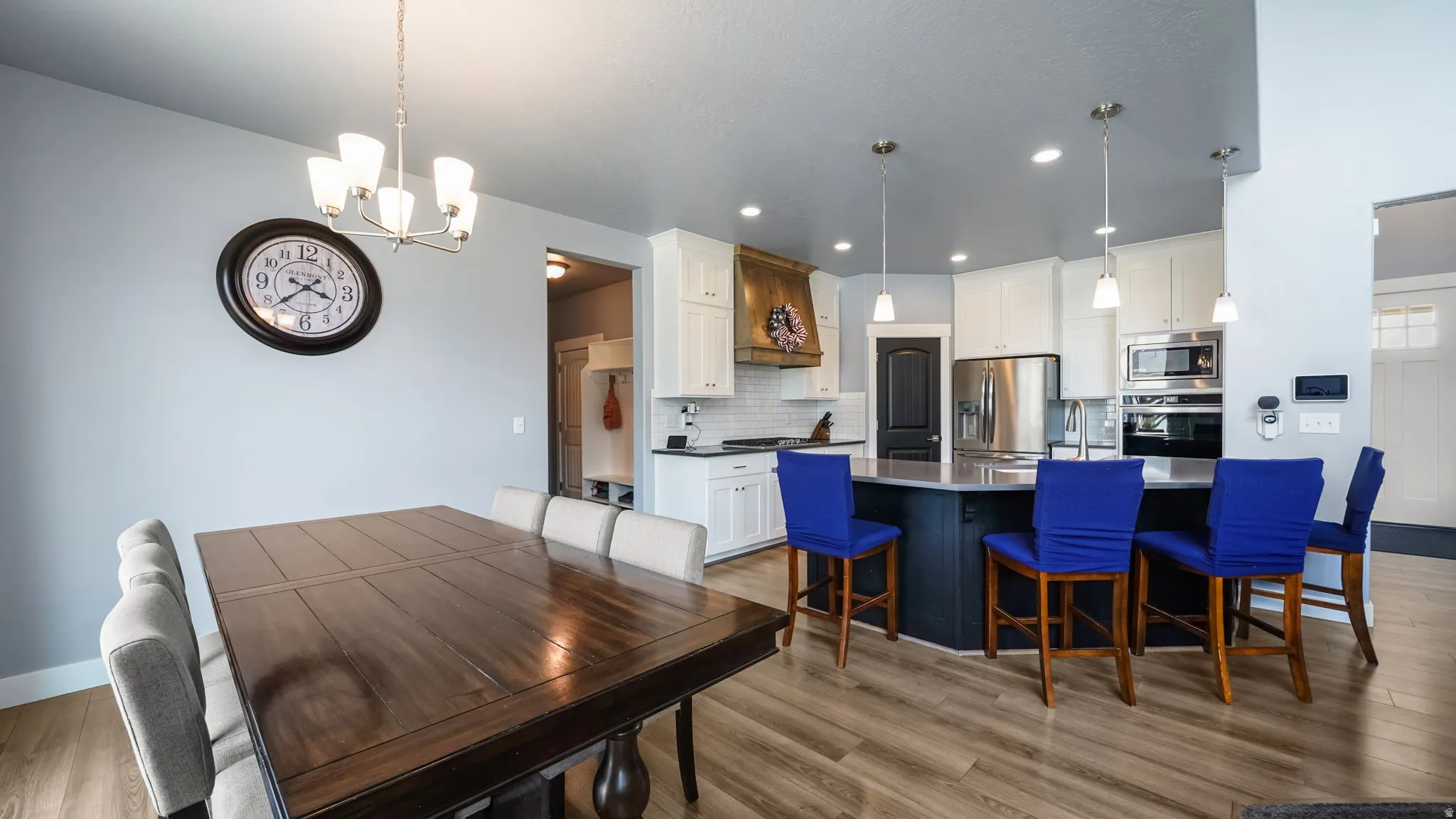Open-concept floor plan featuring wood-finish flooring, a kitchen island with pendant lighting, white cabinetry, and stainless steel appliances