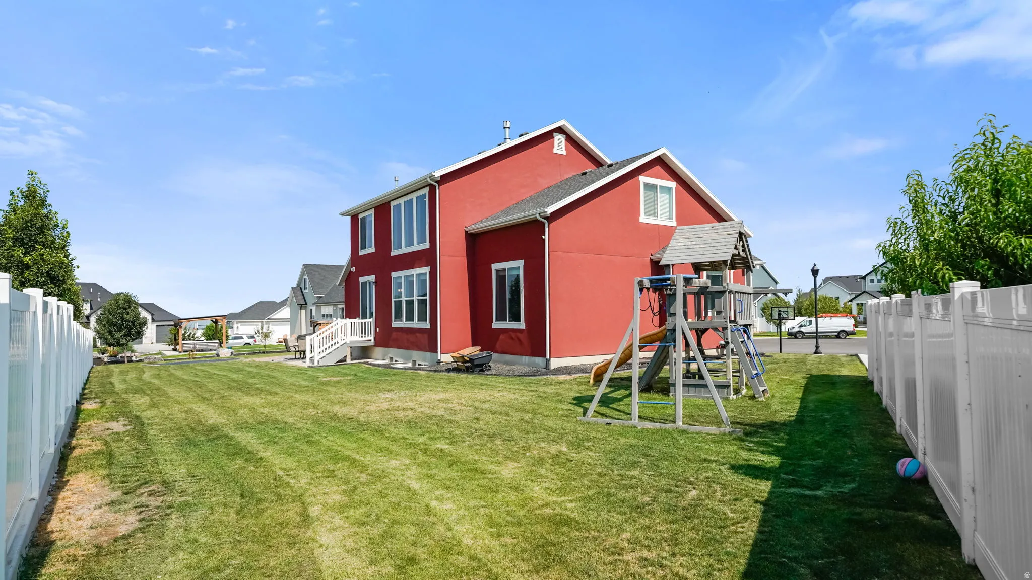 Expansive backyard with a manicured lawn, white privacy fencing, and a two-story exterior with multiple windows