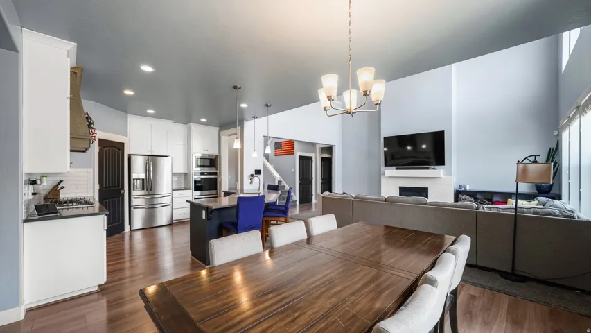 Open-concept living area featuring wood-finish flooring, a kitchen with white cabinetry and stainless steel appliances, a center island, a dining area, and a living room with a fireplace