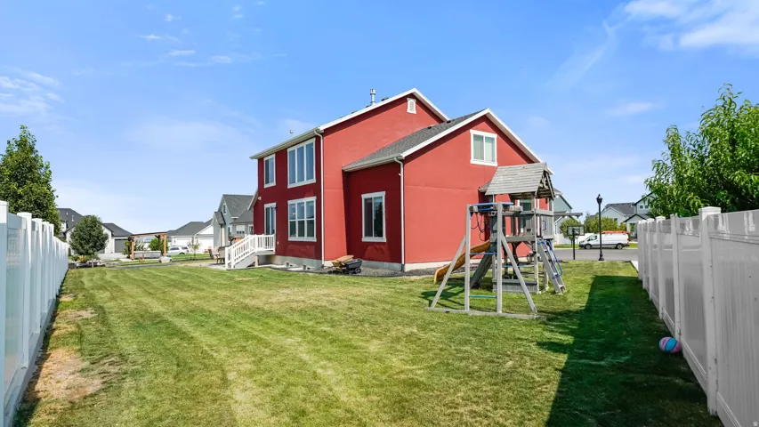 Expansive backyard with a manicured lawn, white privacy fencing, and a two-story exterior with multiple windows