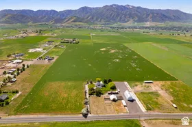 Expansive agricultural land featuring a central residential area, multiple outbuildings, and a paved access road, all set against a backdrop of distant mountains