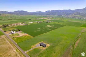 Expansive agricultural land featuring a modern single-family residence, multiple outbuildings, and paved road access