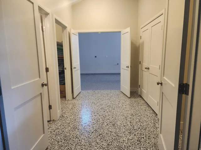 Hallway featuring speckled flooring, white paneled doors, and brushed nickel hardware