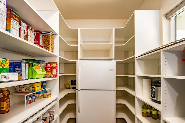 Walk-in pantry featuring extensive built-in shelving, integrated refrigerator, a large window, and recessed lighting