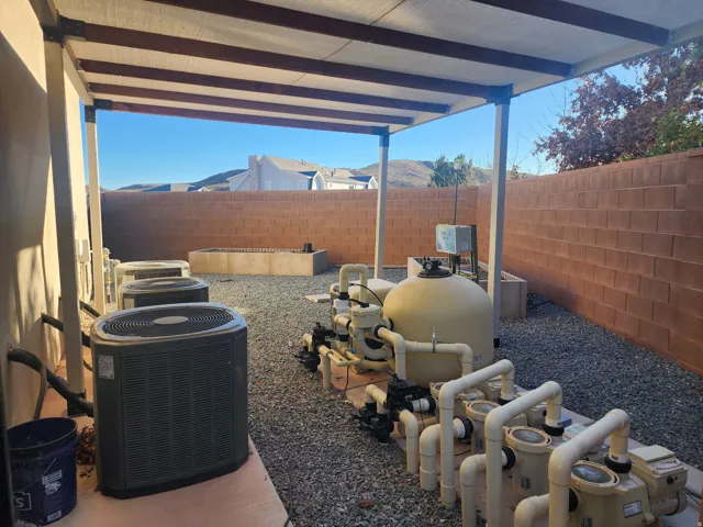 Covered patio area featuring multiple AC units, a pool filtration system, a block privacy wall, and a gravel ground cover