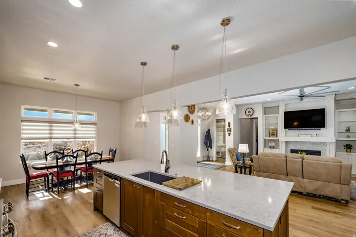 Open-concept living space featuring wood-finish flooring, a kitchen island with stone countertop and integrated sink, pendant lighting, built-in shelving, and a fireplace