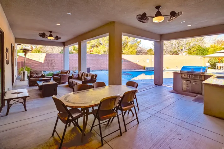 Expansive covered patio featuring an outdoor kitchen with built-in grill, dual ceiling fans, and concrete flooring