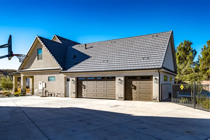 Three-car garage with panel-style doors and exterior sconce lighting, featuring a tiled roof and stucco siding