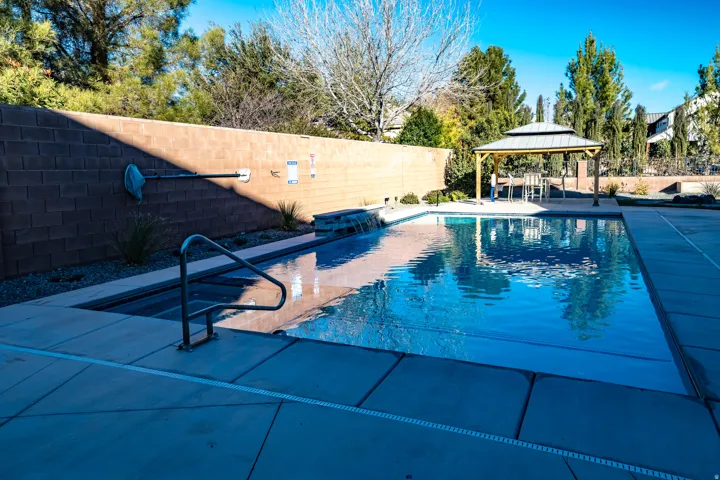 Outdoor swimming pool featuring a waterfall, integrated spa, and surrounding concrete decking