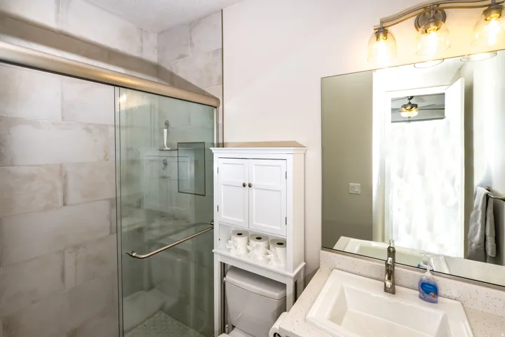 Bathroom featuring a glass-enclosed shower with tile surround, white vanity cabinet, rectangular sink, and a mirrored wall with an overhead three-light fixture