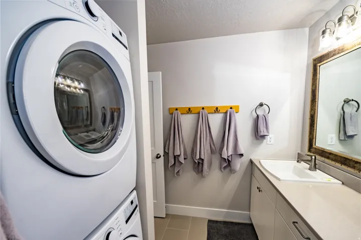 Laundry area featuring a stacked washer and dryer, adjacent to a vanity with integrated sink, light-toned countertop, and modern faucet