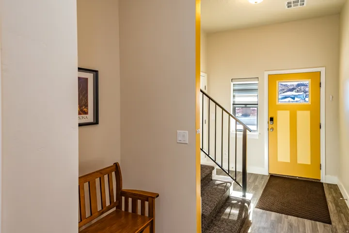 Entryway featuring a bright yellow door with decorative glass, wood-finish flooring, a black metal staircase railing, and a window with blinds