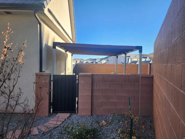 Pergola-covered patio featuring a metal privacy gate, concrete block privacy walls, gravel ground cover, and stepping stones
