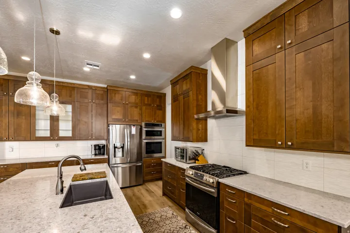 Kitchen featuring extensive wood cabinetry, light-toned countertops, stainless steel appliances, a large island with an undermount sink, and recessed lighting