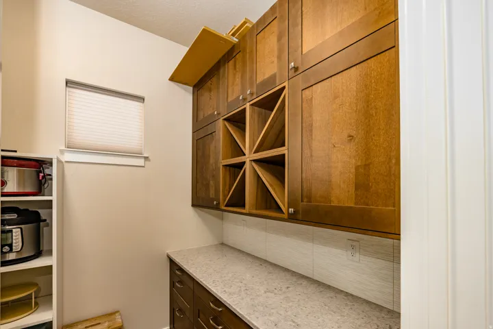 Pantry featuring rich wood cabinetry, integrated wine storage, light-toned countertop, and white subway tile backsplash