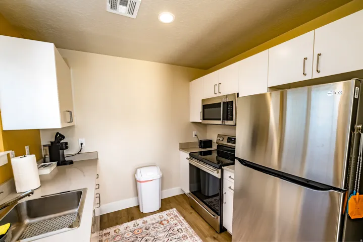Contemporary kitchen featuring white cabinetry, stainless steel appliances, a stainless steel sink, and wood-finish flooring