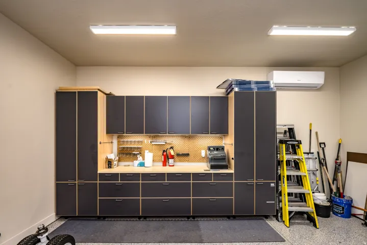 Custom built-in cabinetry with a wood-finish countertop, integrated pegboard, overhead fluorescent lighting, and a wall-mounted mini-split system