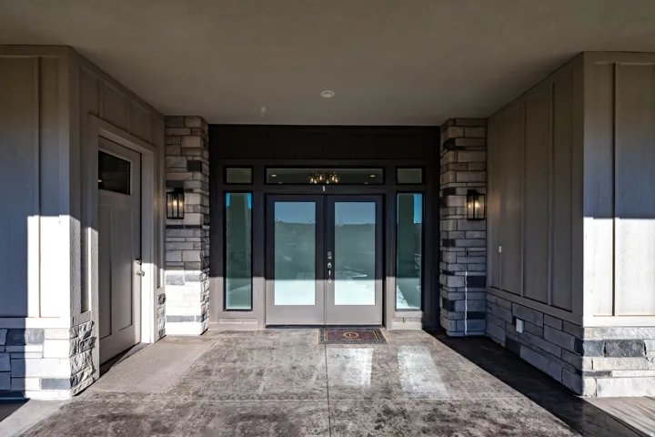 Modern entry featuring double glass doors, stone veneer accents, vertical panel siding, and exterior sconce lighting