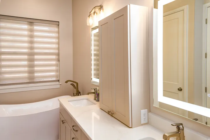 Contemporary bathroom featuring a freestanding soaking tub, dual vanity with undermount sinks, bronze-finish fixtures, and an illuminated mirror