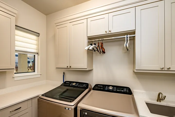 Utility room featuring extensive cabinetry, quartz-finish countertops, a built-in hanging rod, and an undermount sink with a bronze-finish faucet