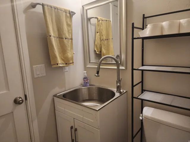 Compact powder room featuring a stainless steel sink with a high-arc faucet, white vanity cabinetry, and a framed wall mirror