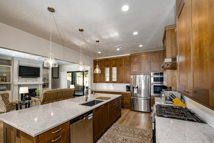 Kitchen featuring wood cabinetry, stainless steel appliances, a center island with a sink, and pendant lighting