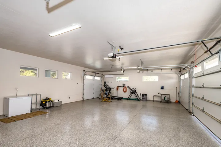 Spacious two-car garage featuring a speckled epoxy floor, multiple windows for natural light, and overhead fluorescent lighting