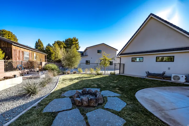 Expansive backyard featuring a central fire pit with stepping stones, a curved concrete patio, and a manicured lawn