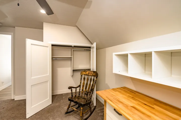 Built-in wooden desk with white cabinetry, overhead open shelving, and a closet with bifold doors