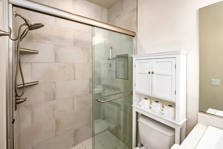 Shower with a brushed nickel showerhead and handheld sprayer, tiled walls, built-in shelving, and hexagonal tile flooring