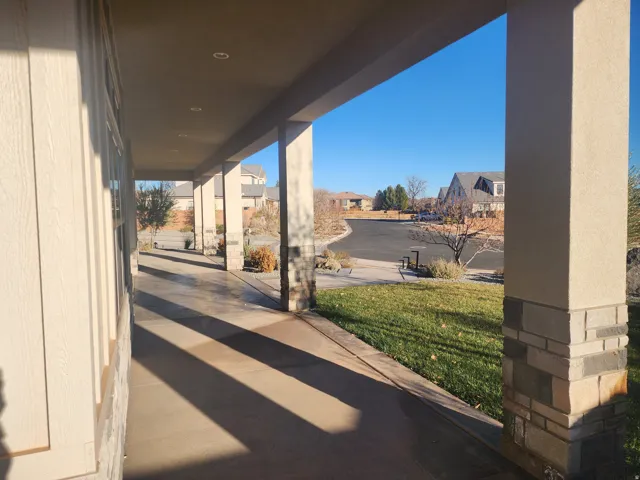 Covered front porch featuring recessed lighting, stone-clad pillars, a paved walkway, and a manicured lawn