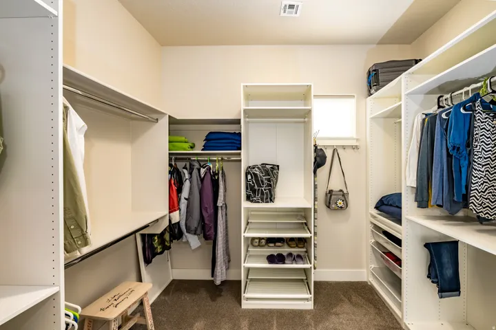 Walk-in closet featuring built-in white shelving, multiple hanging rods, pull-out shoe racks, and ample storage compartments