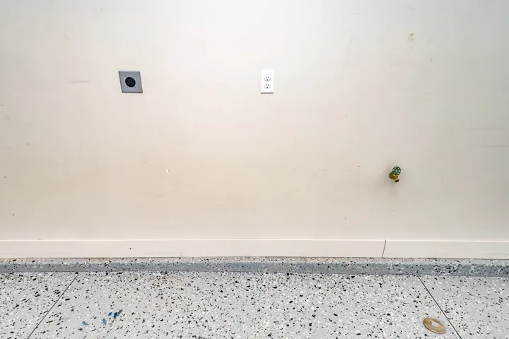 Utility wall featuring electrical outlet, water spigot, and exhaust vent