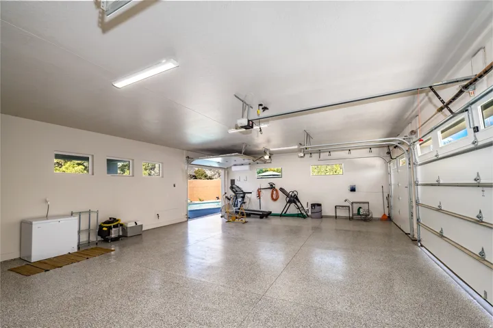 Spacious garage featuring a durable epoxy floor, multiple horizontal windows, overhead fluorescent lighting, and an automatic garage door opener system