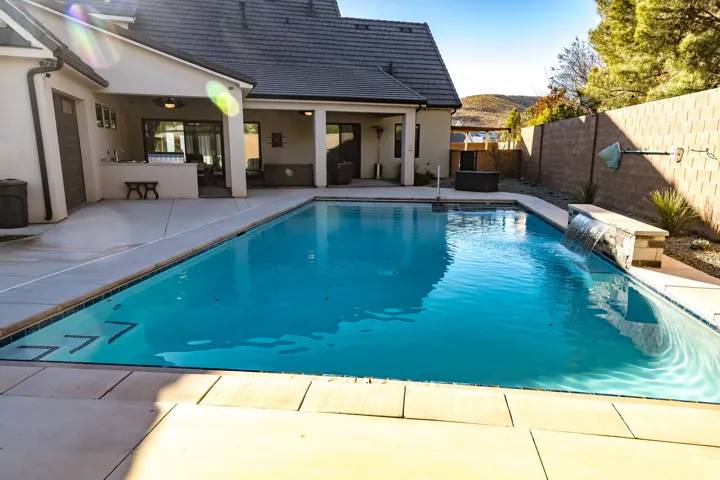 Turquoise swimming pool featuring a waterfall, integrated steps, and surrounding concrete decking