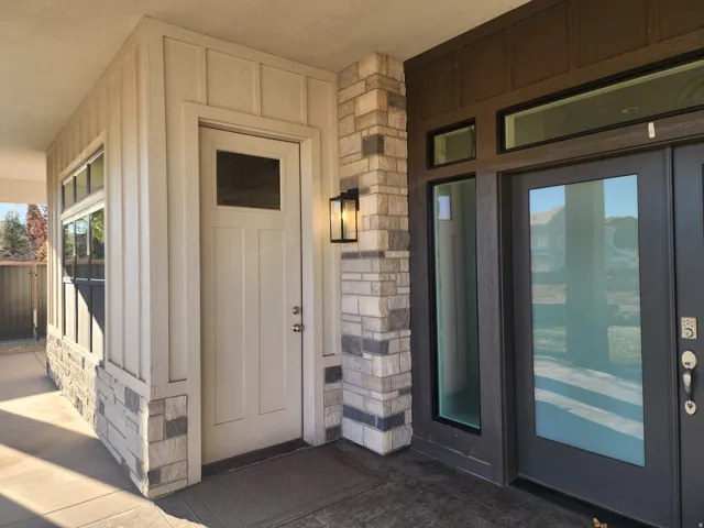 Entryway featuring board and batten siding, stone accents, dual pane windows, a panel door with an integrated window, and a modern exterior light fixture