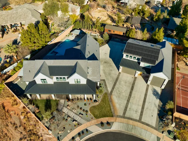 Modern residential complex featuring multiple structures with dark metal roofs, a large swimming pool, and an integrated tennis court