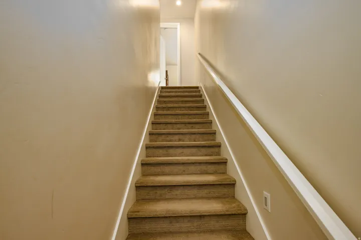 Carpeted staircase with light-toned wall finishes and a white handrail