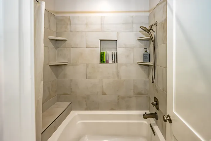 Bathtub with a tiled surround featuring a built-in niche, integrated corner shelving, and a shower seat