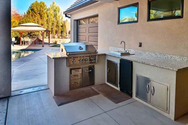 Outdoor kitchen featuring a built-in stainless steel grill, integrated sink, and granite countertops