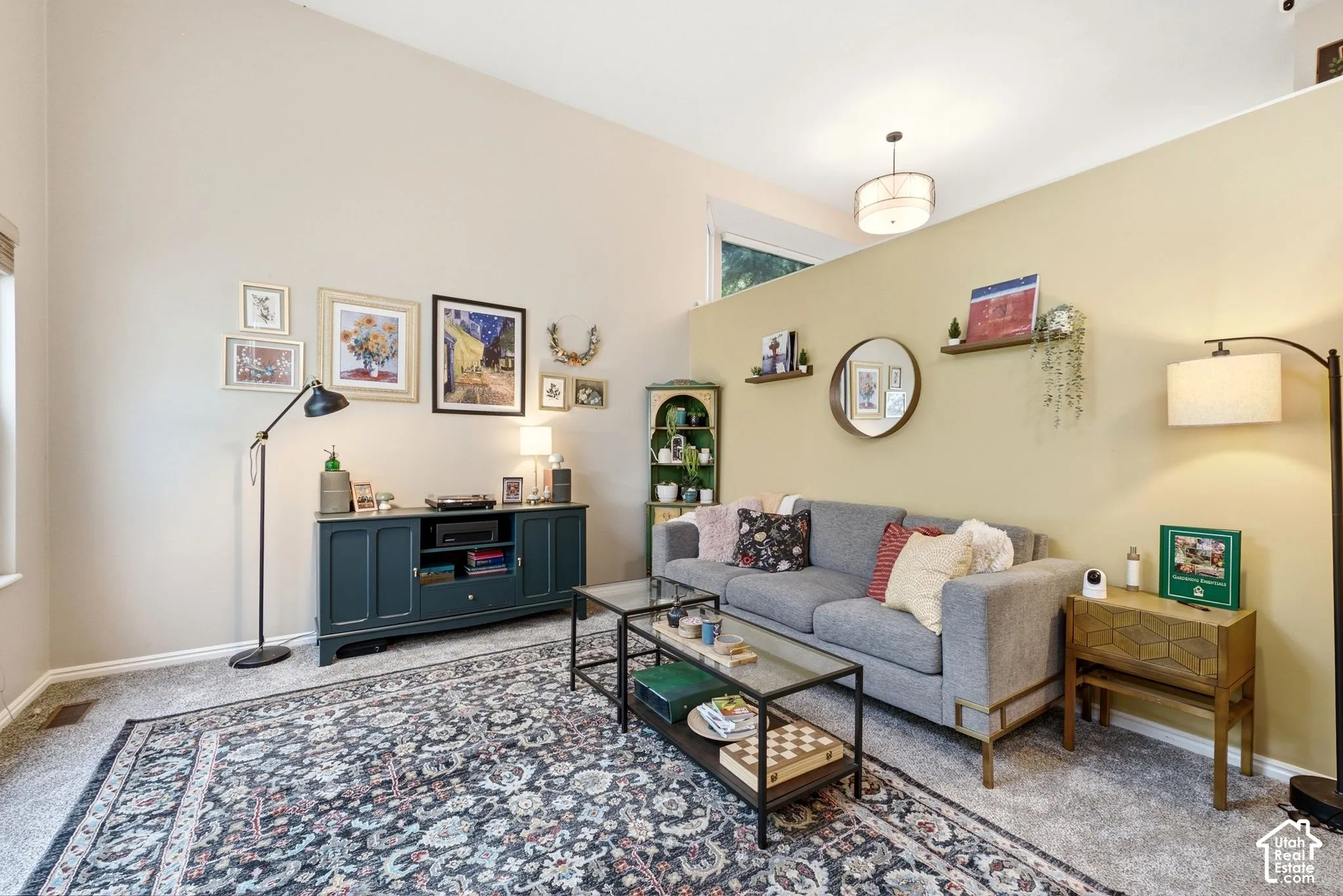 Vaulted ceiling living space featuring a window, carpeted flooring, and a partial wall with an overhead light fixture