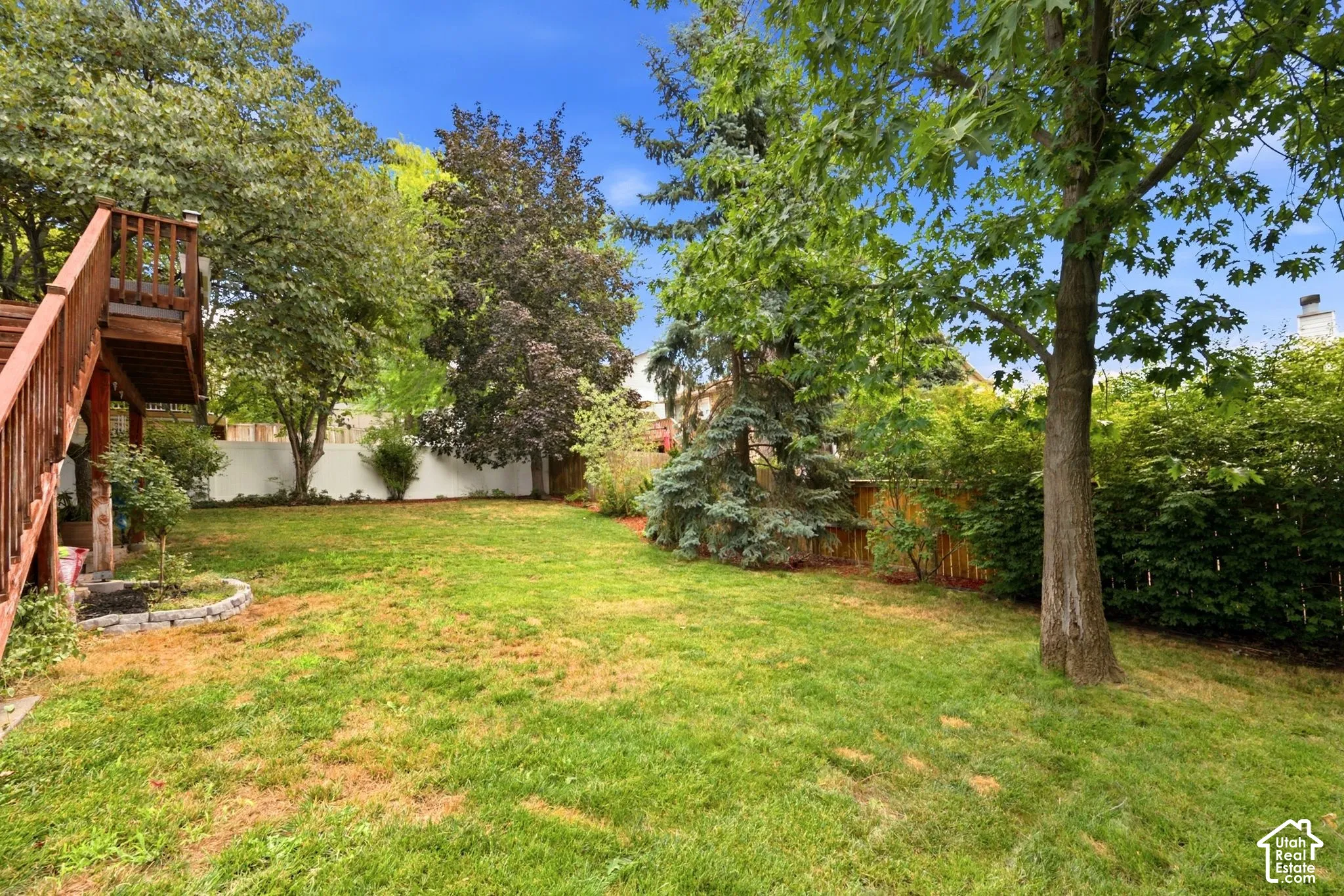 Spacious backyard featuring a multi-level wood deck, established trees, and a stone-edged garden bed