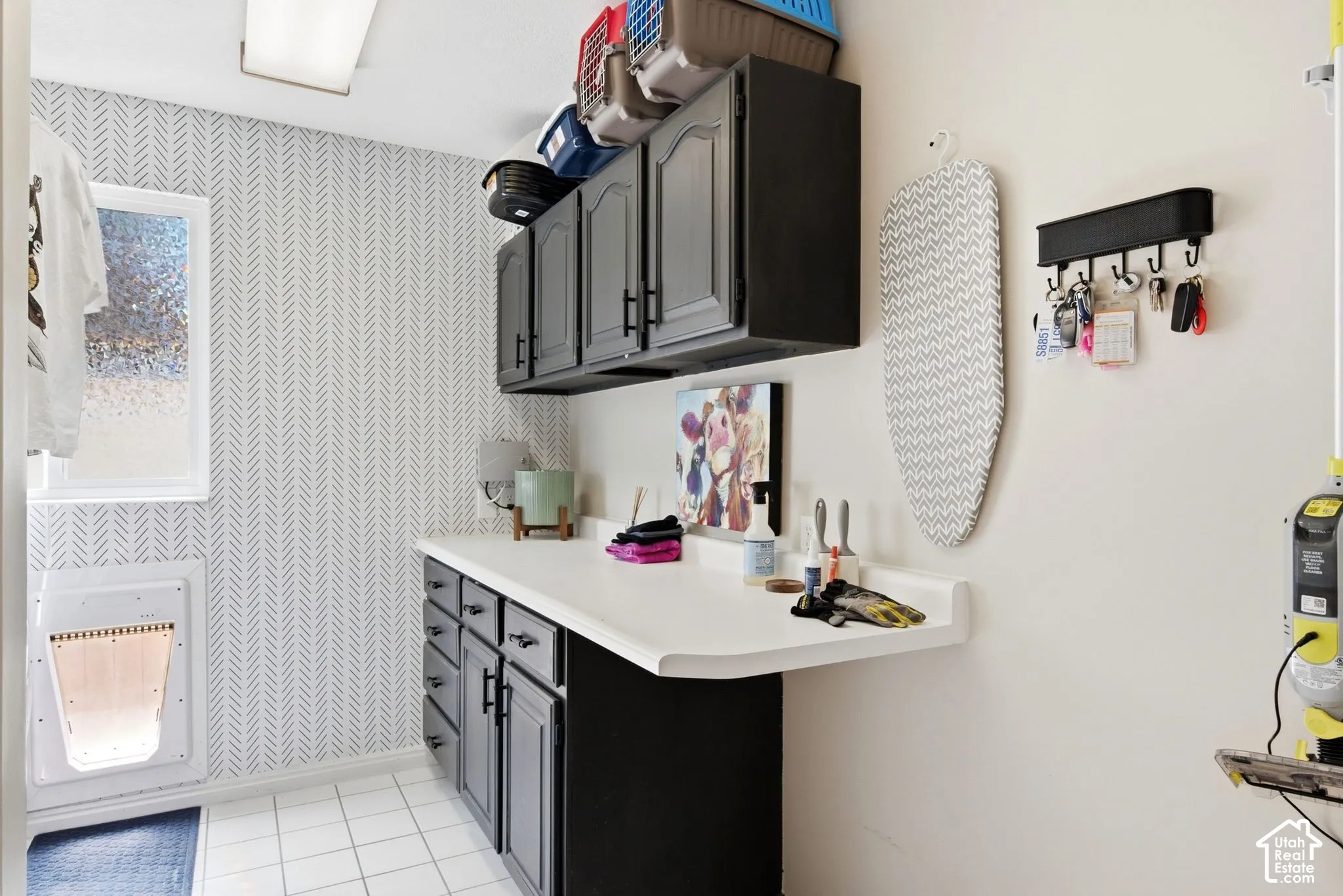 Utility room featuring patterned wallpaper, white tile flooring, dark cabinetry, and white countertops