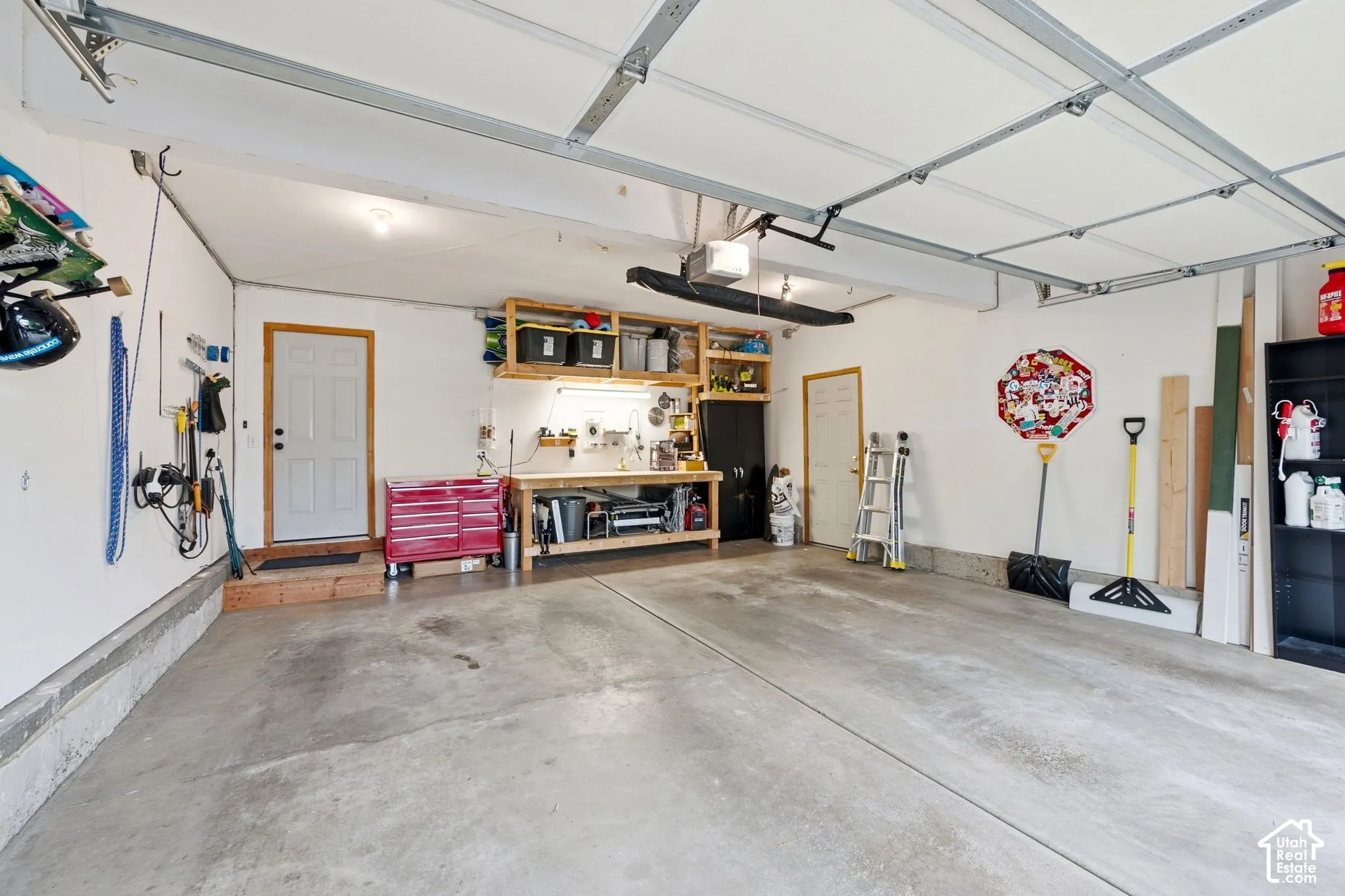 Spacious garage with exposed beam ceiling, concrete flooring, built-in shelving, and workbench area