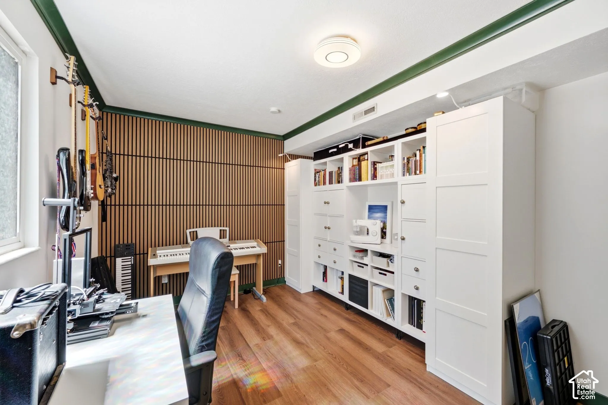 Office space with wood-finish flooring, a full wall of custom built-in cabinetry, slatted wood accent wall, and a large window