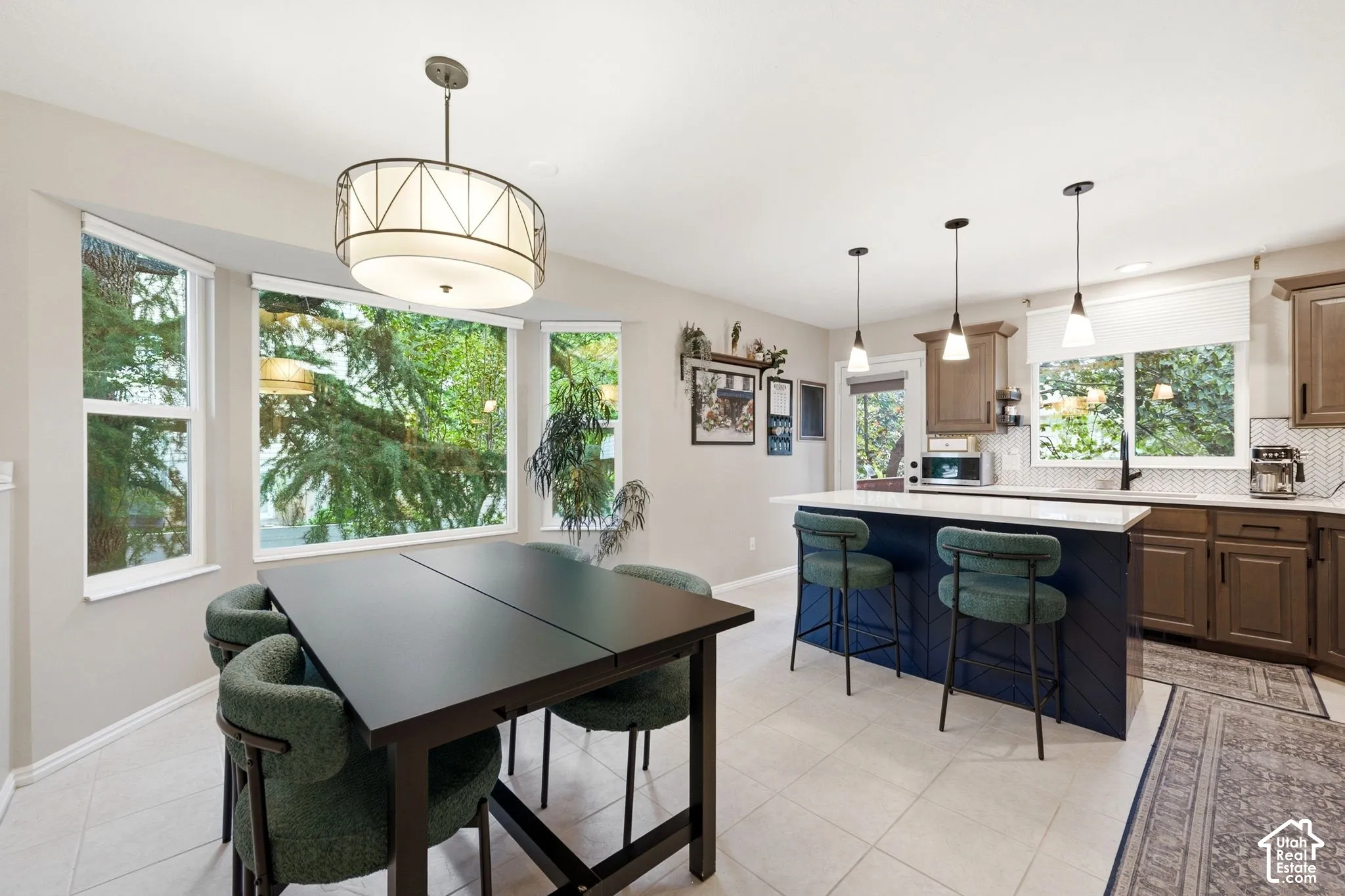 Open-concept kitchen and dining area featuring a bay window, light tile flooring, a kitchen island with seating, a white countertop, and pendant lighting