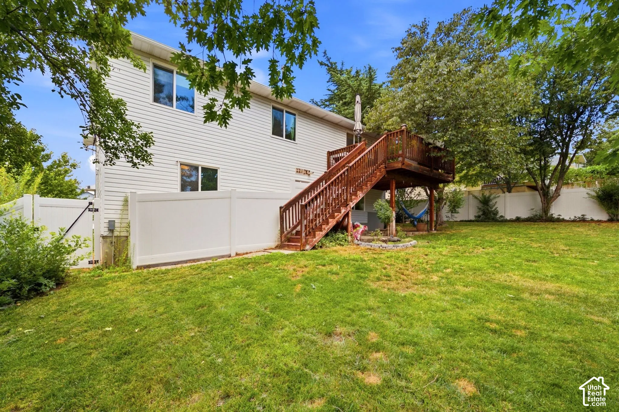 Spacious backyard featuring a large wooden deck with stairs, white vinyl fencing, and a manicured lawn