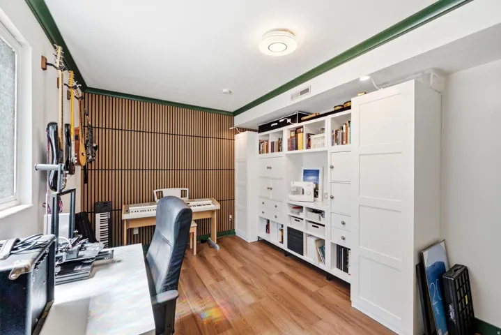 Office space with wood-finish flooring, a full wall of custom built-in cabinetry, slatted wood accent wall, and a large window